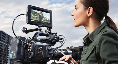 Woman operating a camera with a monitor displaying a scene outdoors.